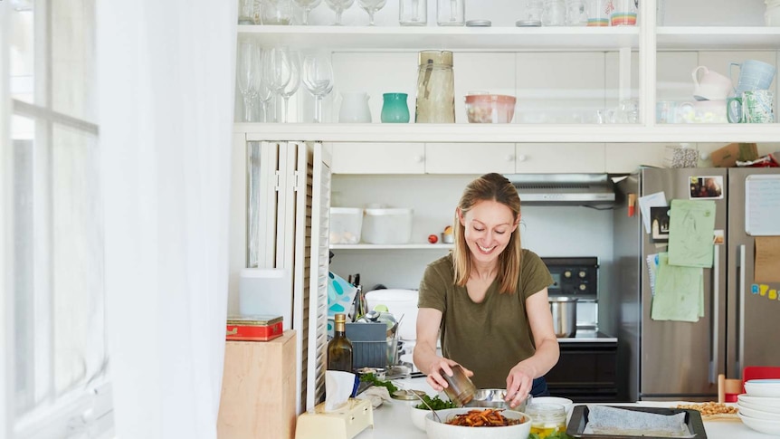 A woman smiles as she dresses a grain salad in her kitchen at home, preparing to take it to a family gathering.