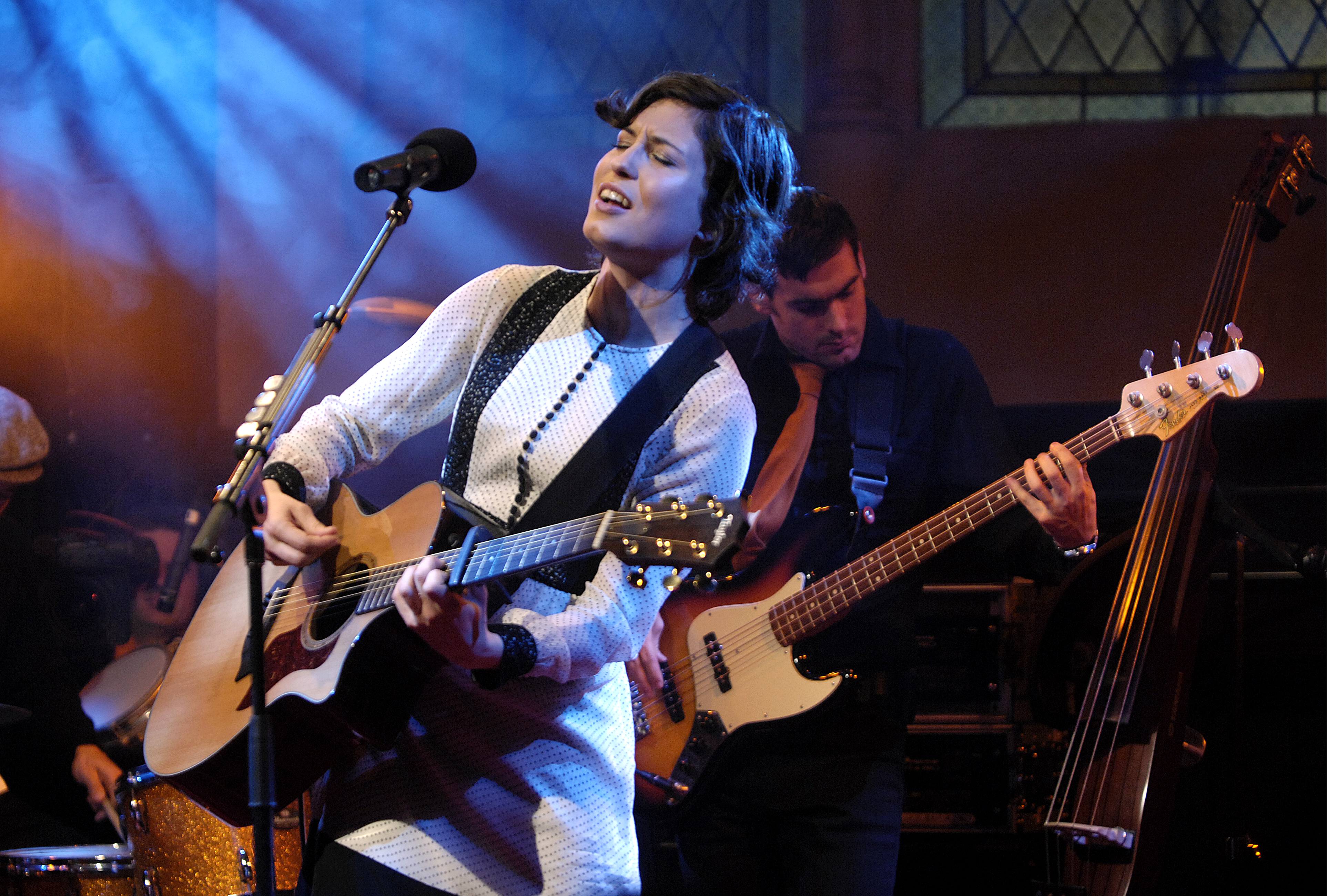 Missy Higgins wearing a white dress on stage holding a guitar 