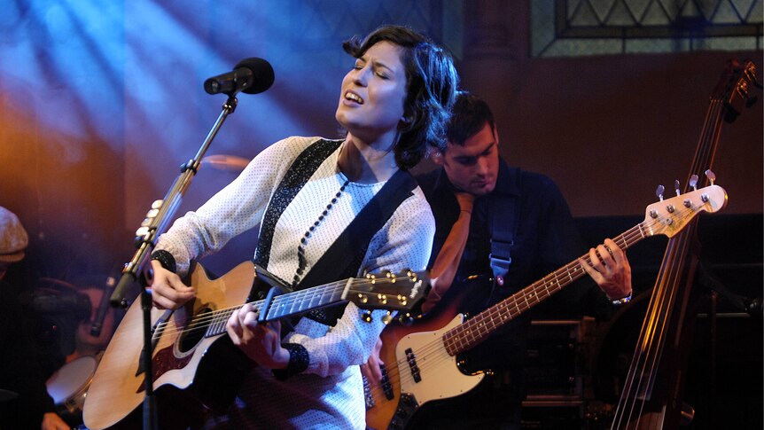 Missy Higgins wearing a white dress on stage holding a guitar 