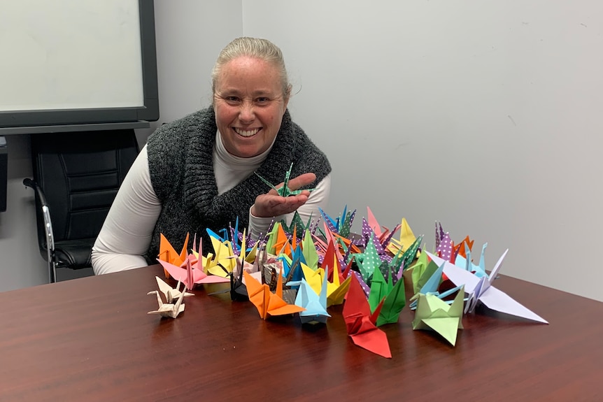 A lady in a gray jumper sitting with some paper cranes in front of her. 