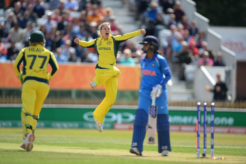 Kristen Beams leaps in the air and yells while batter Mithali Raj walks off the pitch.