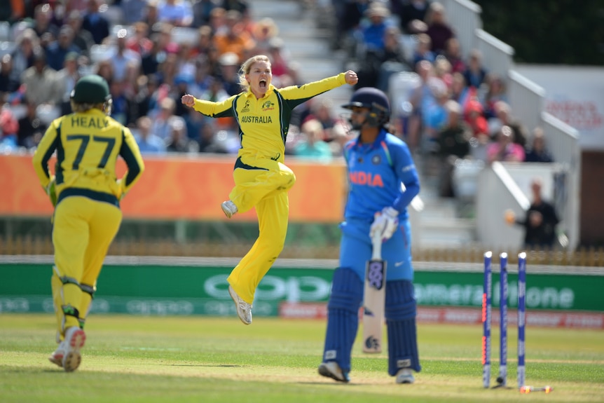 Kristen Beams leaps in the air and yells while batter Mithali Raj walks off the pitch.