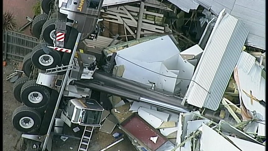 Sheets of twisted metal surround a fallen crane between two houses.
