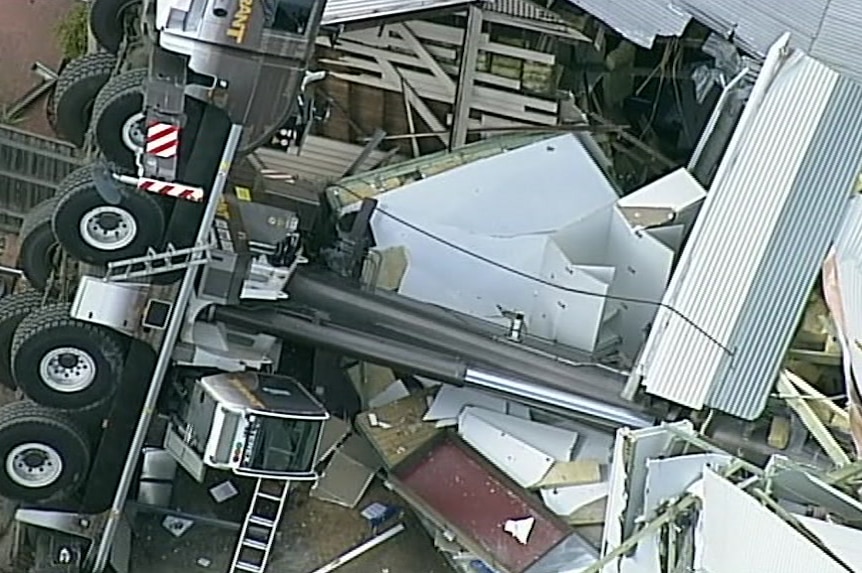 Sheets of twisted metal surround a fallen crane between two houses.