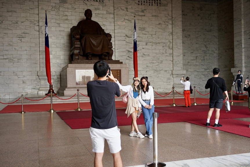 Two young women pose before a giant bronze statue 