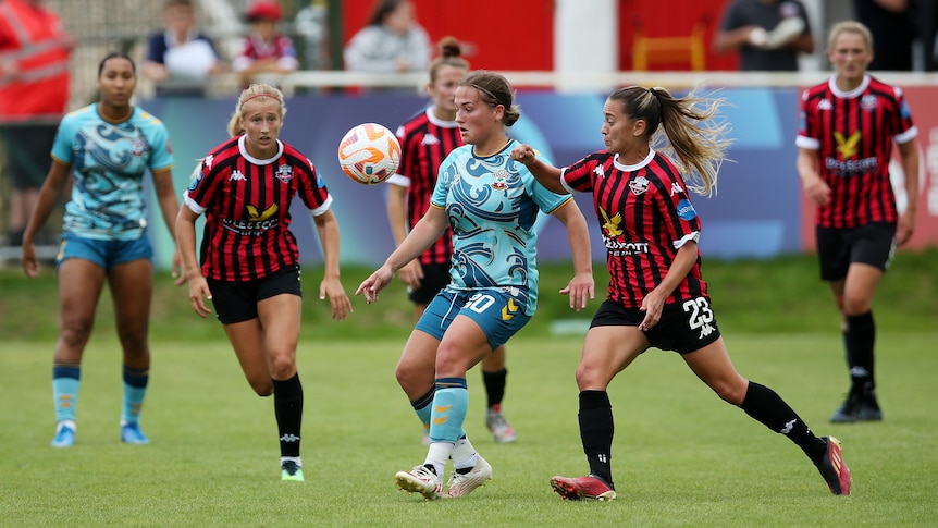 Two soccer teams, one wearing red and black stripes and the other wearing blue waves, during a match