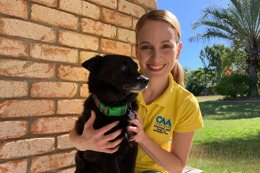 A woman wearing a yellow polo shirt holding a black dog