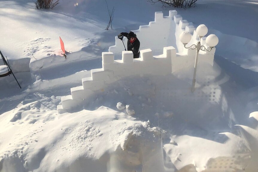 A person builds a castle-shaped structure out of snow.