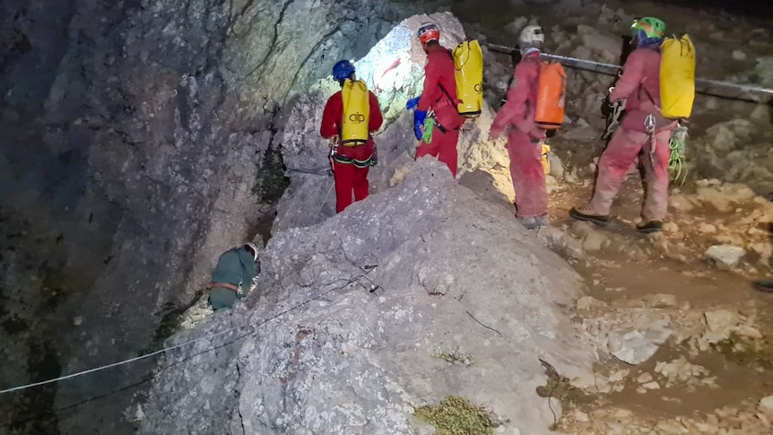 A cave rescue team warring helmets and overalls descends into a cave using a rope