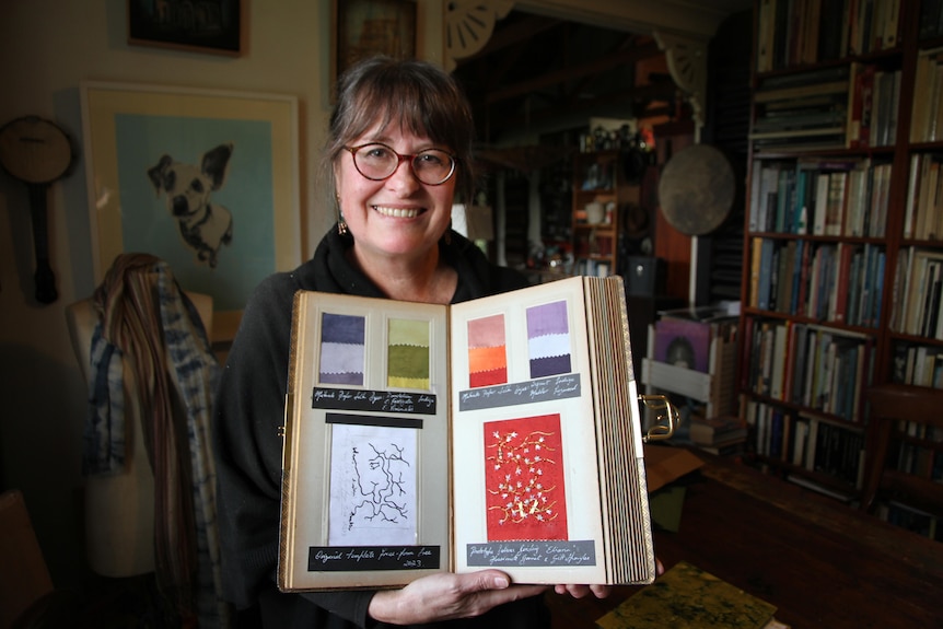 A woman holds a large book she made with scraps and details from her artistic process. 