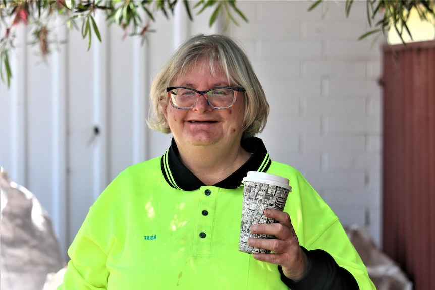 She has chin length hair and wears a fluro top. She holds a takeaway coffee cup