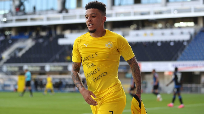 A footballer in Germany runs away from goal showing 'Justice for George Floyd' on his T-shirt.