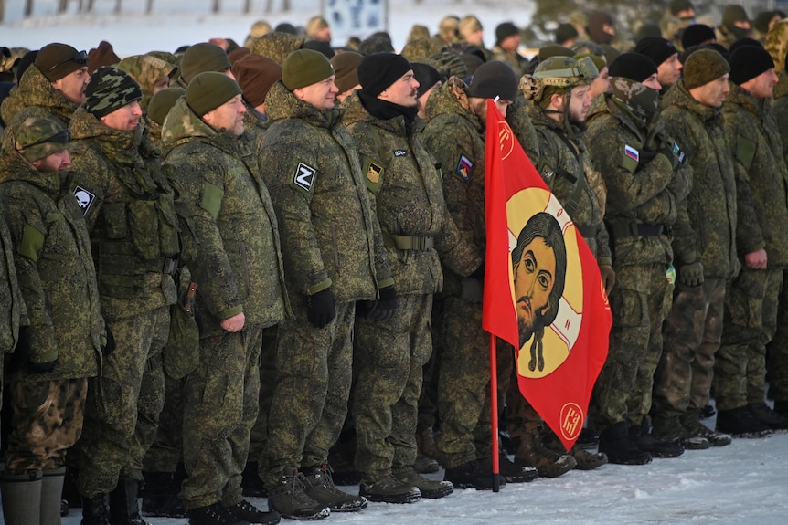 Dozens of Russian reservists stand in a row, wearing thick winter military jackets.