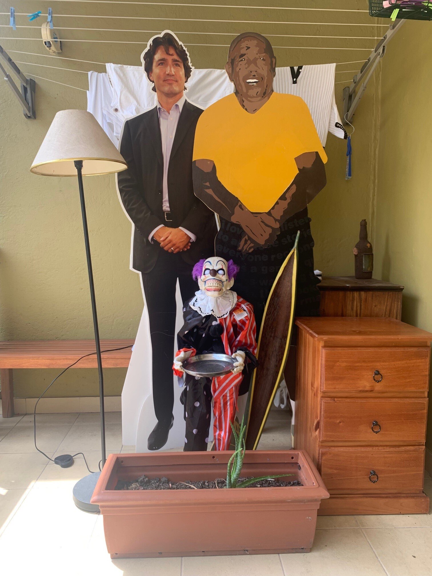 A white lampshade, cutouts of Justin Trudeau and a 'painting-like' Barack Obama, potted plant, clown figurine, drawers.