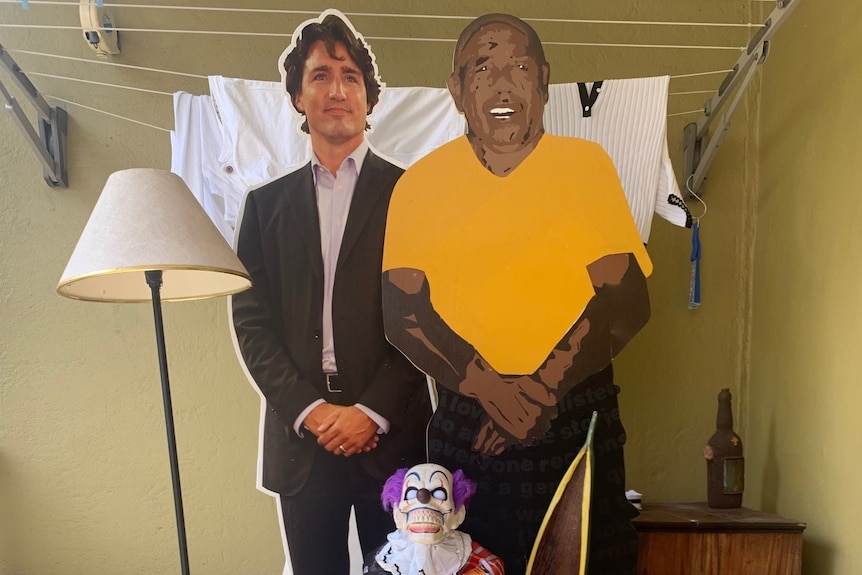 A white lampshade, cutouts of Justin Trudeau and a 'painting-like' Barack Obama, potted plant, clown figurine, drawers.