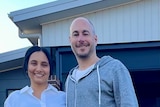 Man and woman smiling, standing side by side in front of their home