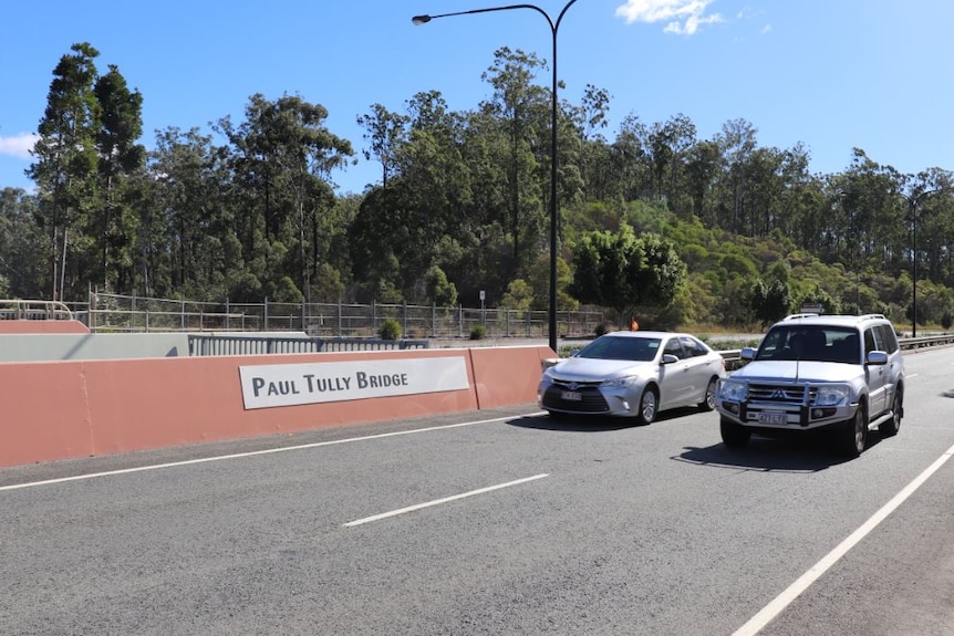 Cars drive past a sign on a bridge that says 'Paul Tully Bridge'.