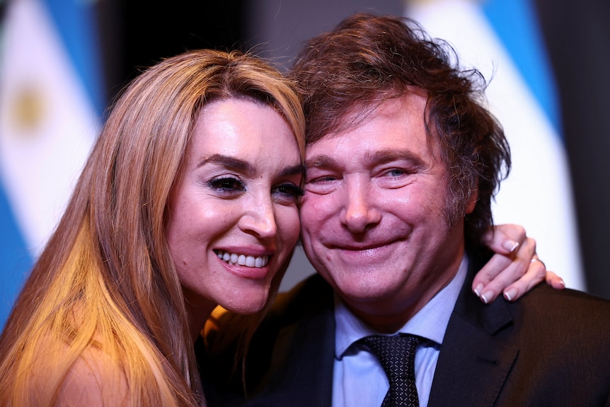 A woman with blonde hair smiles next to a man with floppy hair.