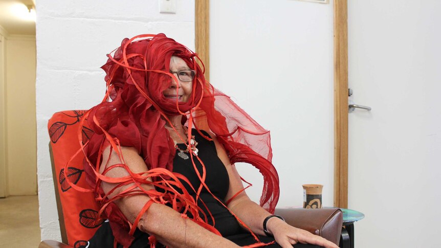 A woman sitting in a chair wearing an elaborate flowing red headpiece.