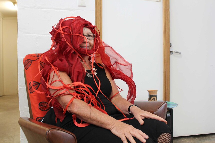 A woman sitting in a chair wearing an elaborate flowing red headpiece.