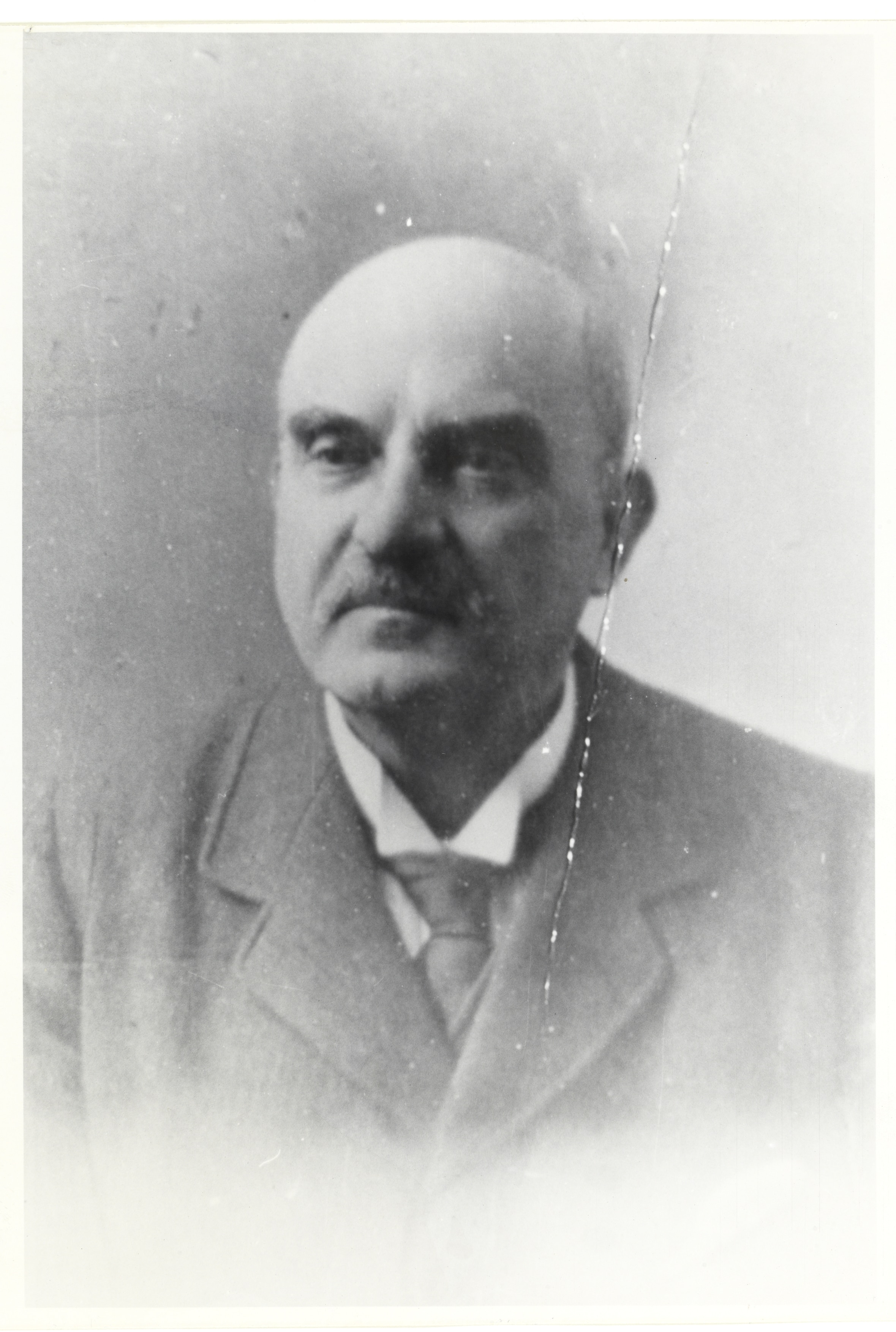 Man in suit, with bald head, thick eyebrows and mustache