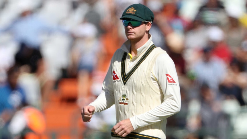 An Australian cricketer stands on the ground wearing his Baggy Green and dark glasses.