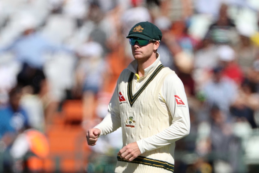 An Australian cricketer stands on the ground wearing his Baggy Green and dark glasses.