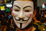 A protester hides his face behind a Guy Fawkes mask