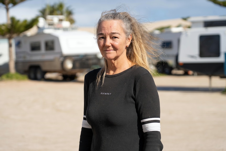 A woman wearing a black jumper looks impassively towards the camera.