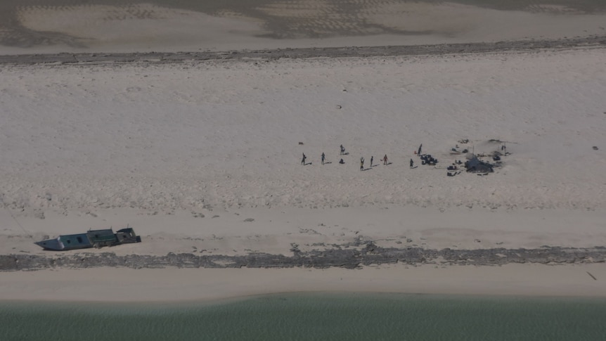 An overhead shot of a group of people on a beach with boat washed up