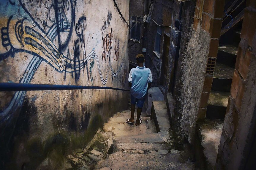 A man walks down stairs between crowded homes and buildings covered with graffiti