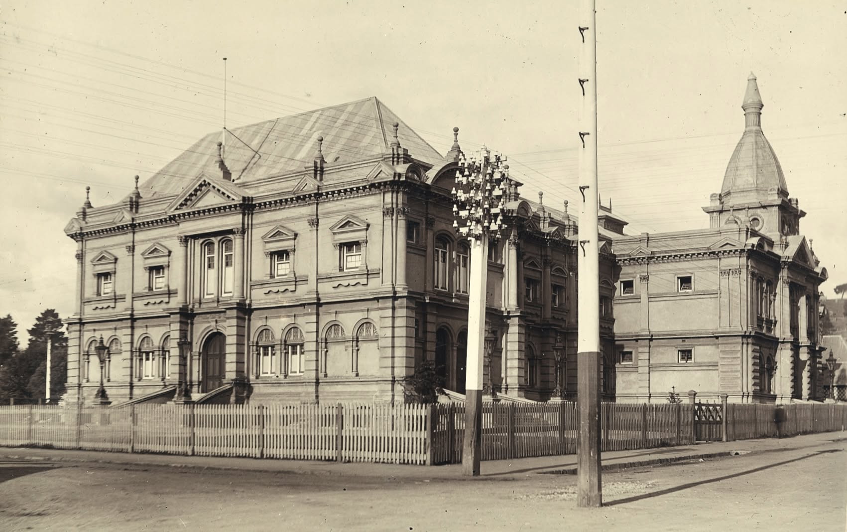 A black and white picture of a grand Victorian-era building with a fence