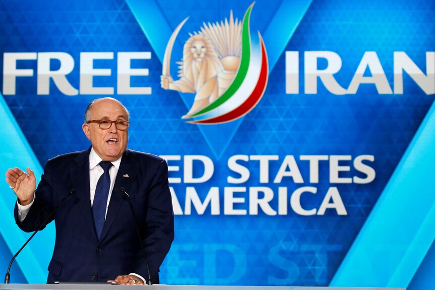Rudy Giuliani gestures while giving a speech, with "Free Iran" written on screens in the background.
