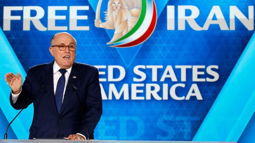 Rudy Giuliani gestures while giving a speech, with "Free Iran" written on screens in the background.