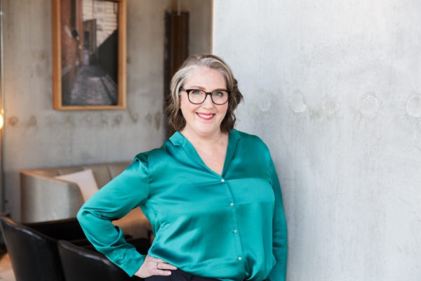 Uma mulher com uma blusa de seda sorrindo para a câmera com a mão no quadril