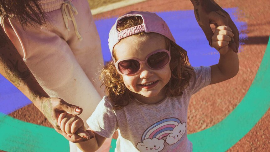 A young girl wearing sunglasses smiles while an adult holds her hands for a story about sharing photos of kids on social media.