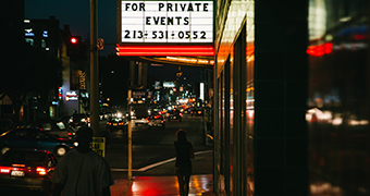 A woman stands outside a nightclub in Los Angeles at night.