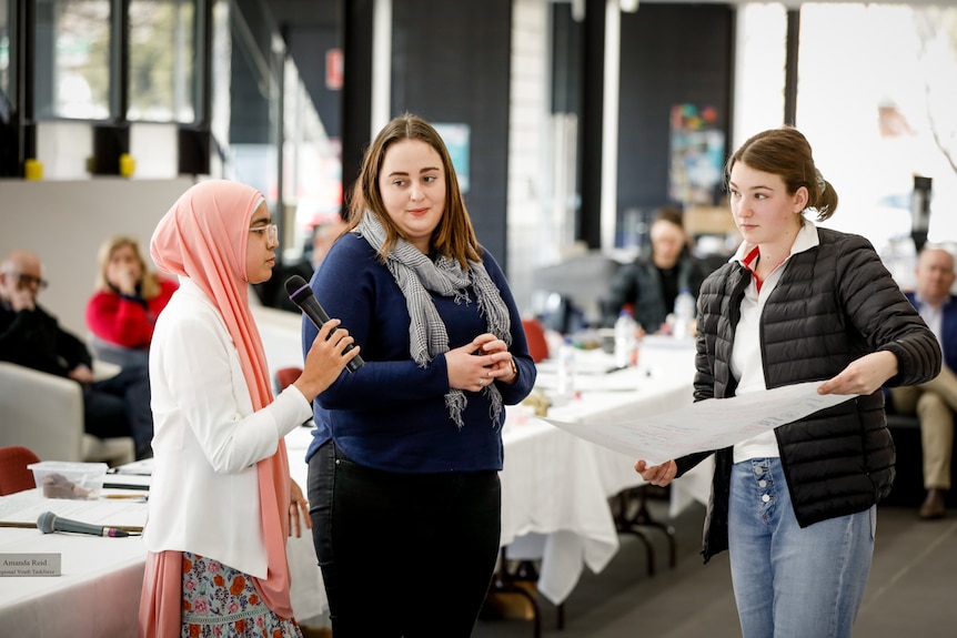 Girl holding microphone alongside two other girls.