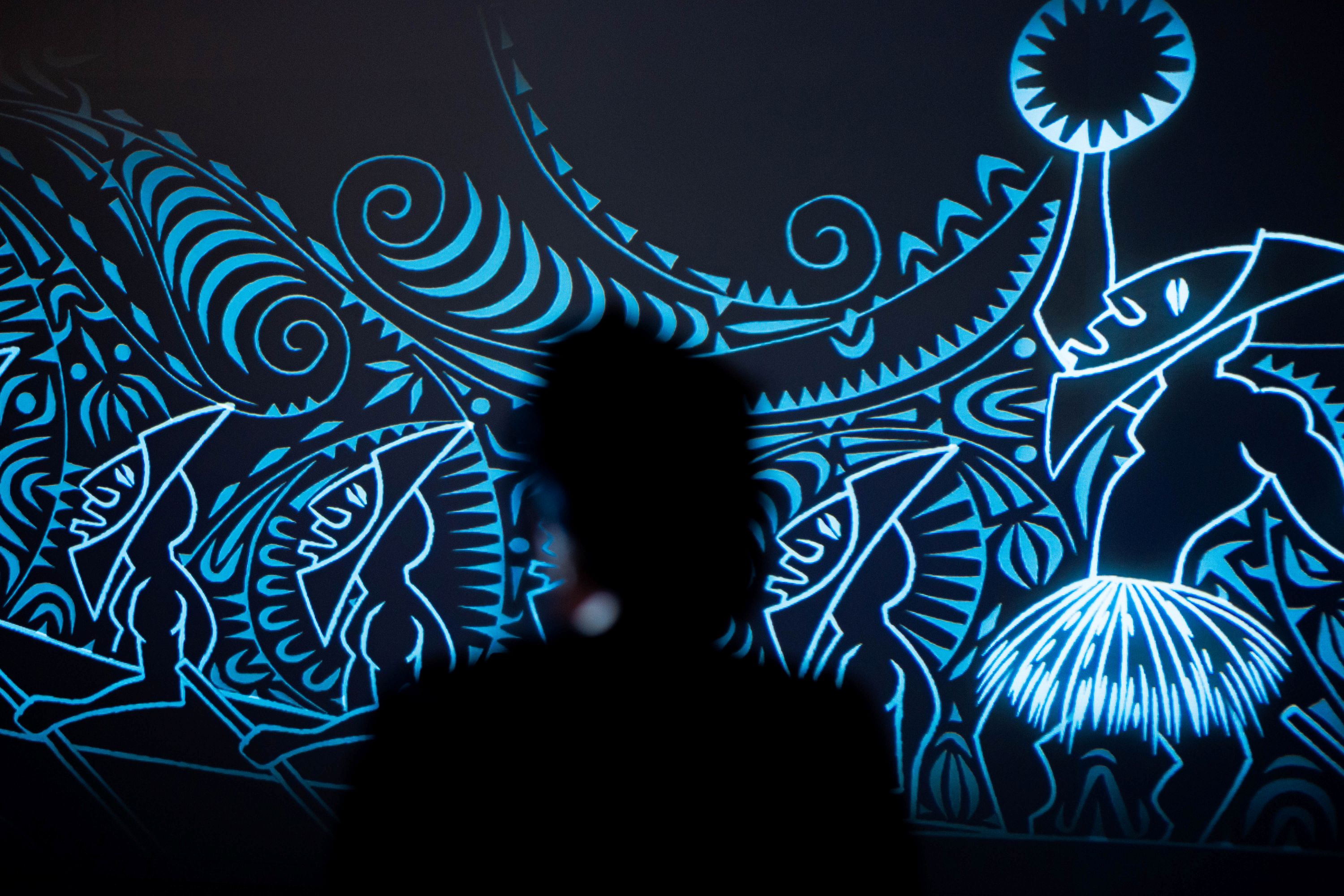 Una silueta de una persona mirando una instalación de arte estampada e iluminada en azul.