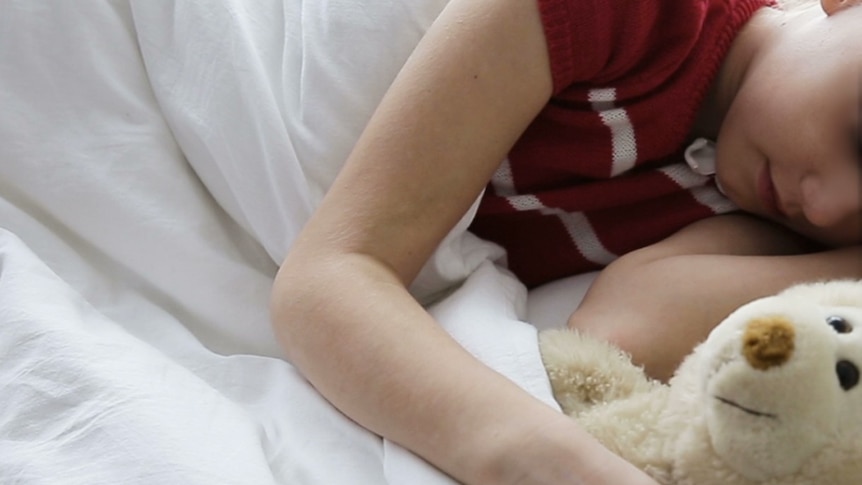 A child is asleep with a teddy.