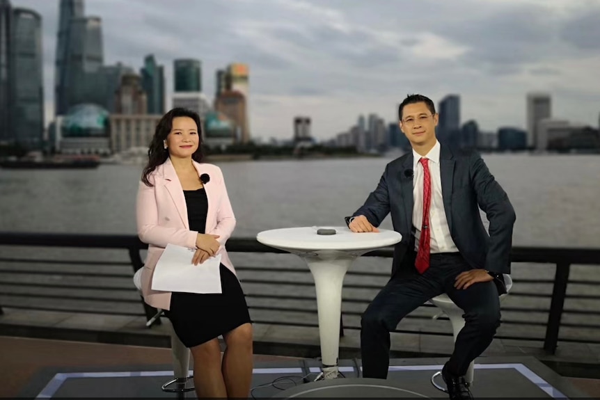 A China woman and a Chinese man sitting at a table with the Shanghai skyline behind them