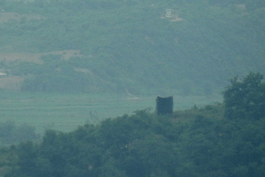 A speaker sits atop a hill with green countryside surrounding the area.