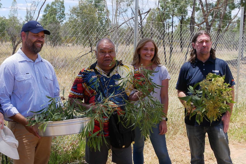 Five people standing with wattle seed branches.