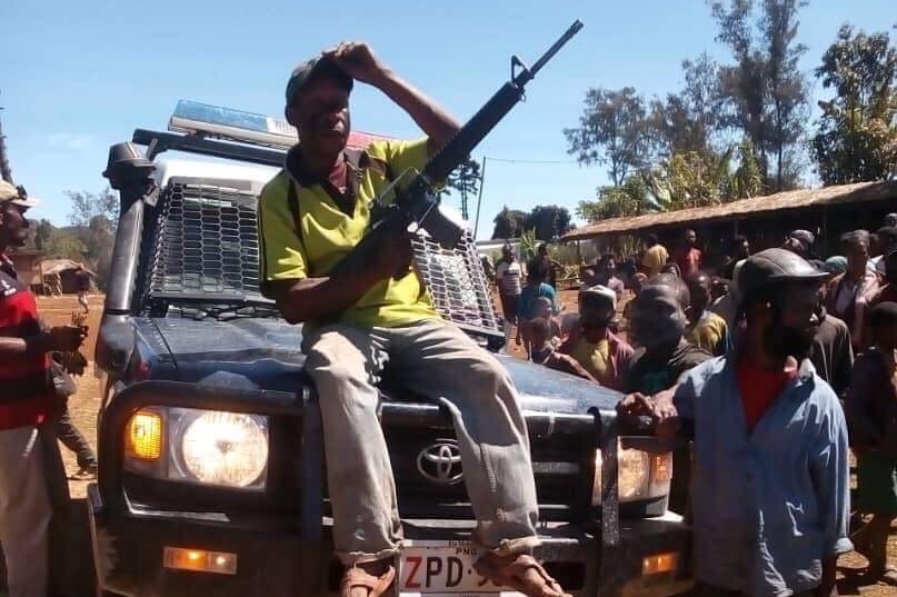 A man sits on a car holding a gun
