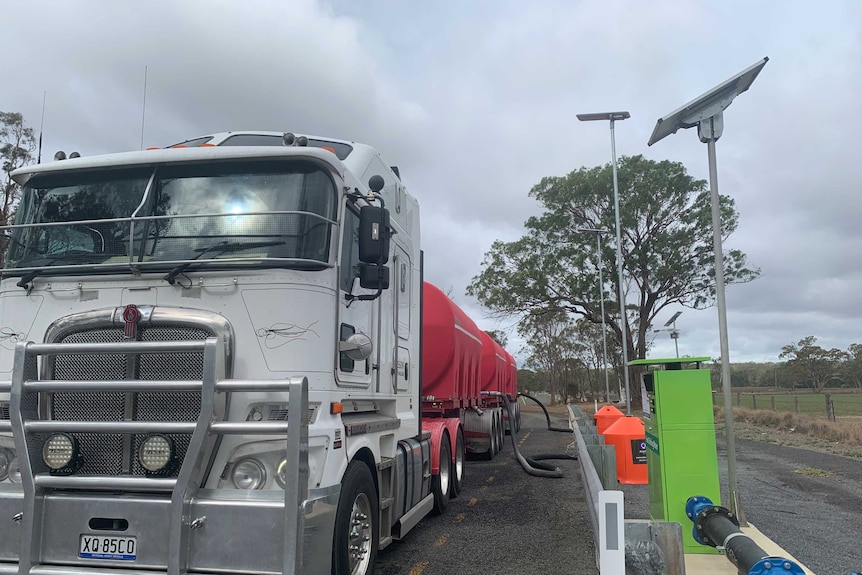 A truck is parked next to water pump, where pipes move water into storage containers.