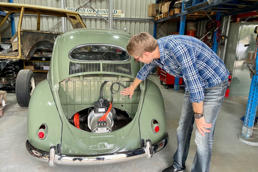 A man leans over the back of a Beetle leaning over the back of a car being converted.