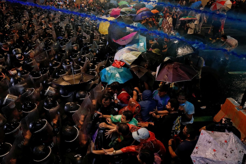 Electric blue water with tear gas shot from a water cannon flies over demonstrators during a Bangkok protest.