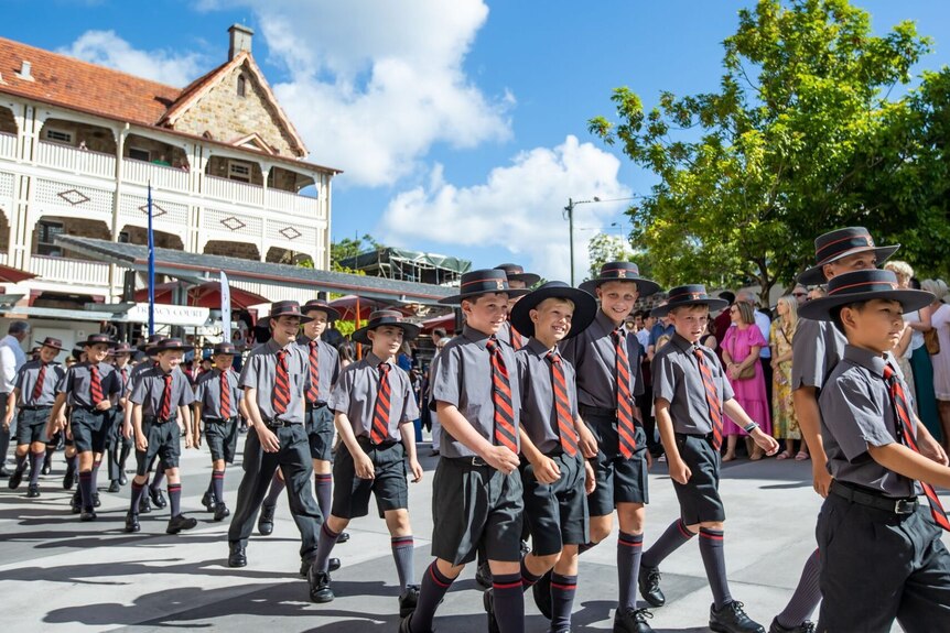 A crowd of boys in school uniforms - ties, shorts and long socks - walk along a concrete path.