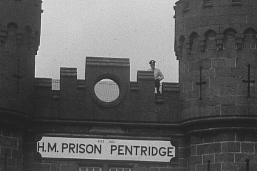 A historical black-and-white image of a prison guard looking over the gates of Victoria's Pentridge Prison.