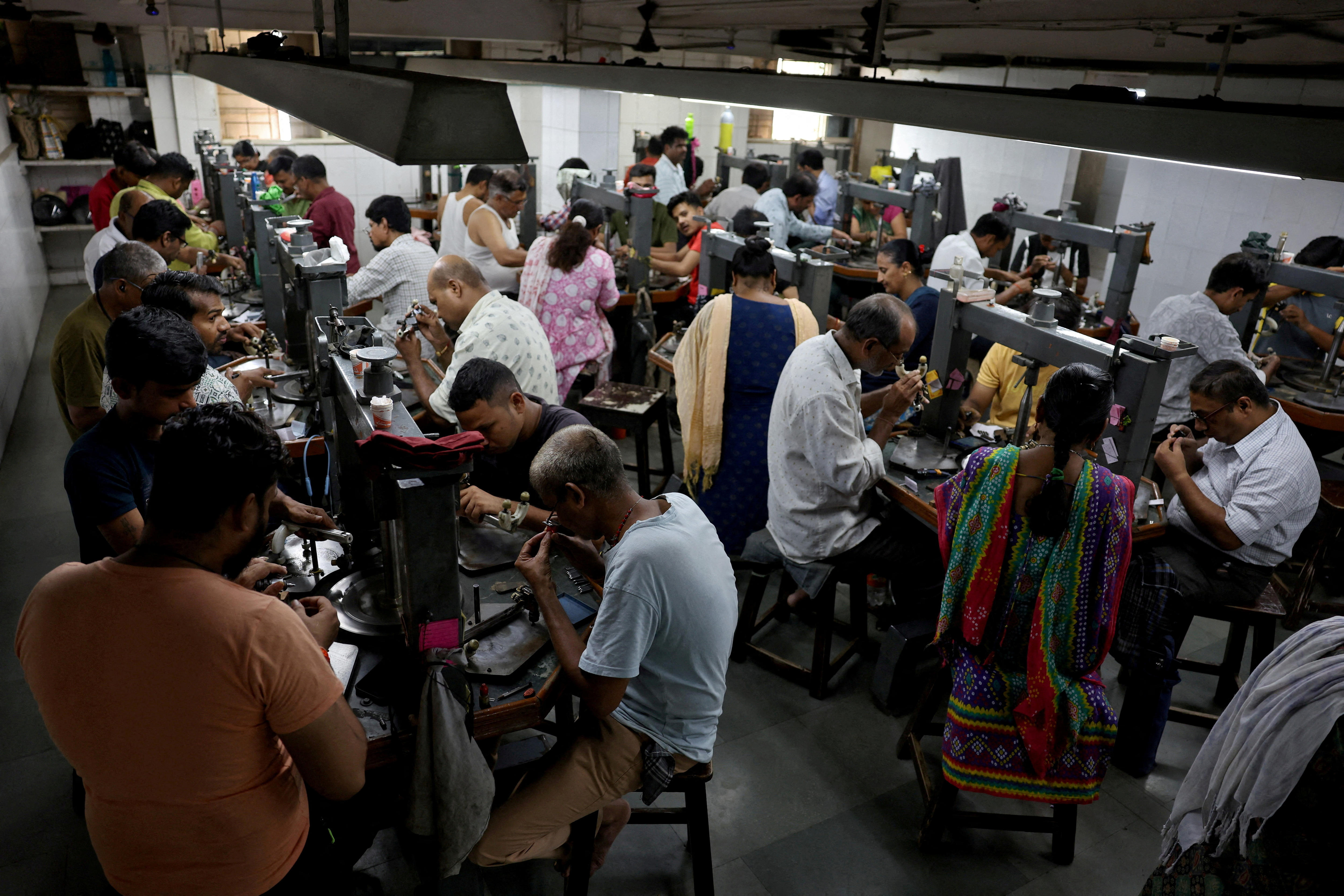 Dozens of people sit on long benches polishing small gem stones under bright white lights